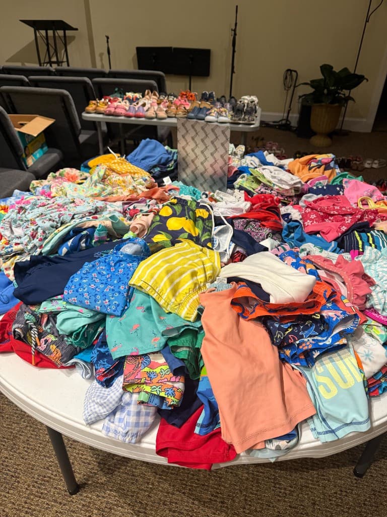 Table overflowing with baby and toddler onesies and outfits