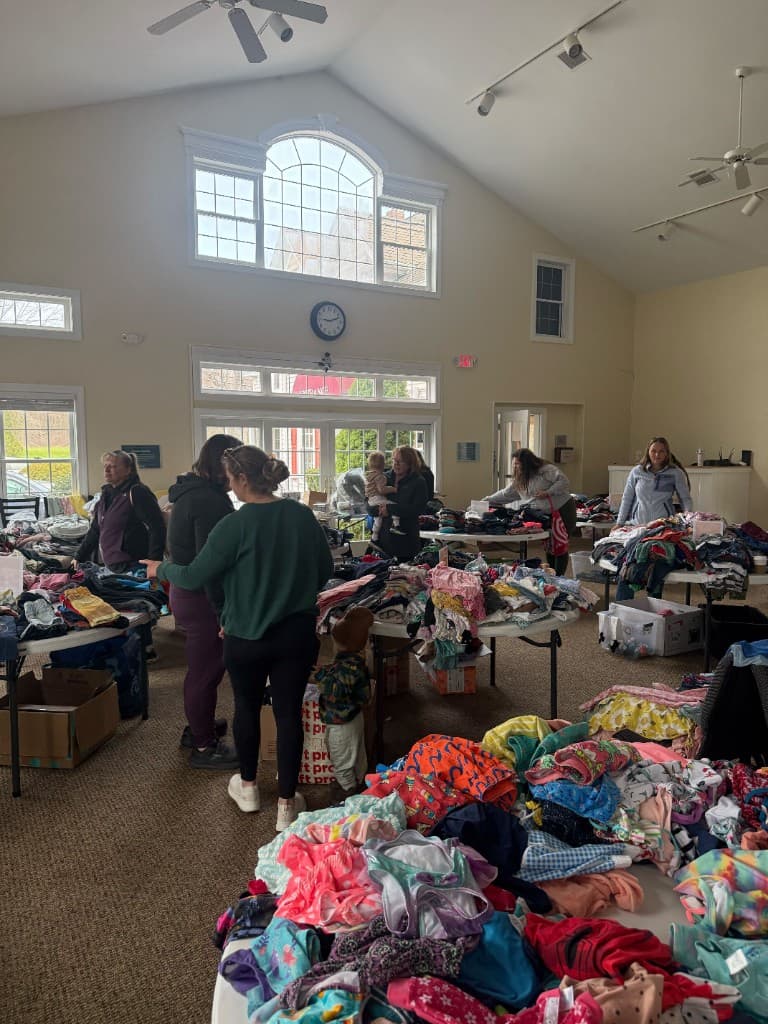 Volunteers and families gathered around round tables of sorted children's clothes