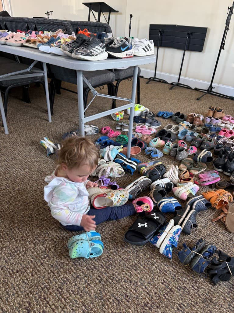 Toddler sitting on the floor surrounded by donated children's shoes